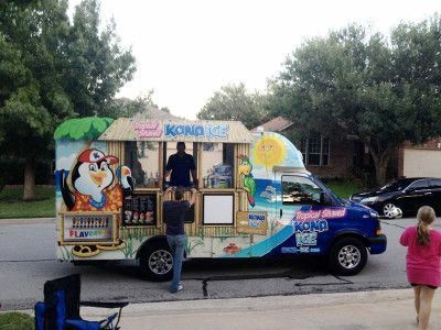 Kona Ice truck with cartoon graphics parked on a residential street; person taking order.