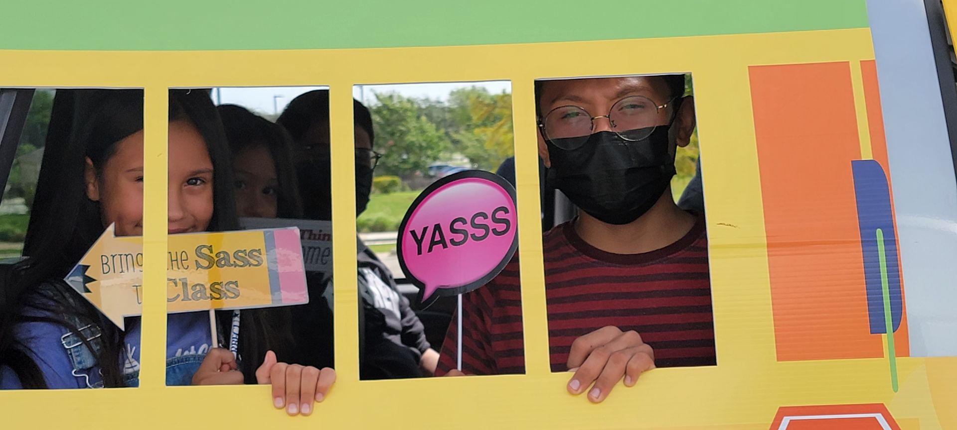 People posing in front of a school bus cutout, holding signs: 