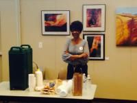 Woman stands behind a table with coffee and snacks in an art gallery, surrounded by framed artwork.