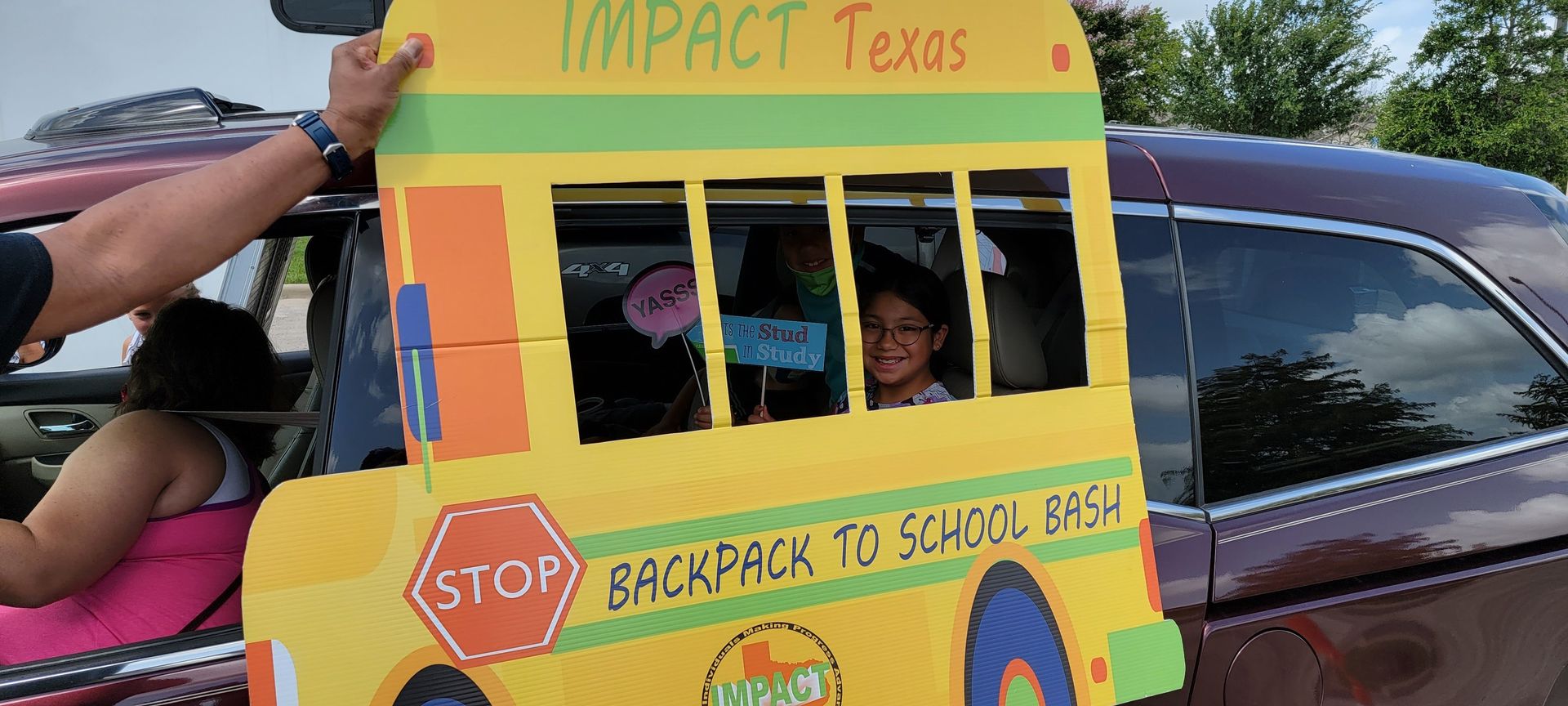 Person holding a yellow school bus cutout with a child smiling in the window of a car.