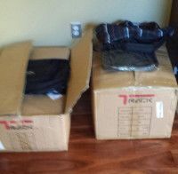 Two cardboard boxes on wooden floor, one open, both with black items inside.