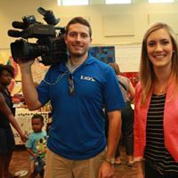 Man with camera on shoulder, two women, and a child smiling in a bright room.