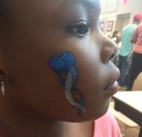 Close-up of a person's face with a blue and silver face paint design.