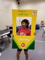 Girl poses with a crayon-shaped photo frame that says 