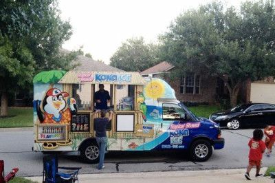 Kona Ice truck parked on a residential street; customers ordering; colorful tropical design; person taking picture.