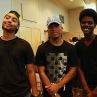 Three young men smiling, wearing black shirts. One has a cap, another a yellow headband.