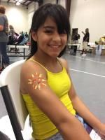 Girl with a sun-shaped temporary tattoo on her arm smiles while sitting in a room.