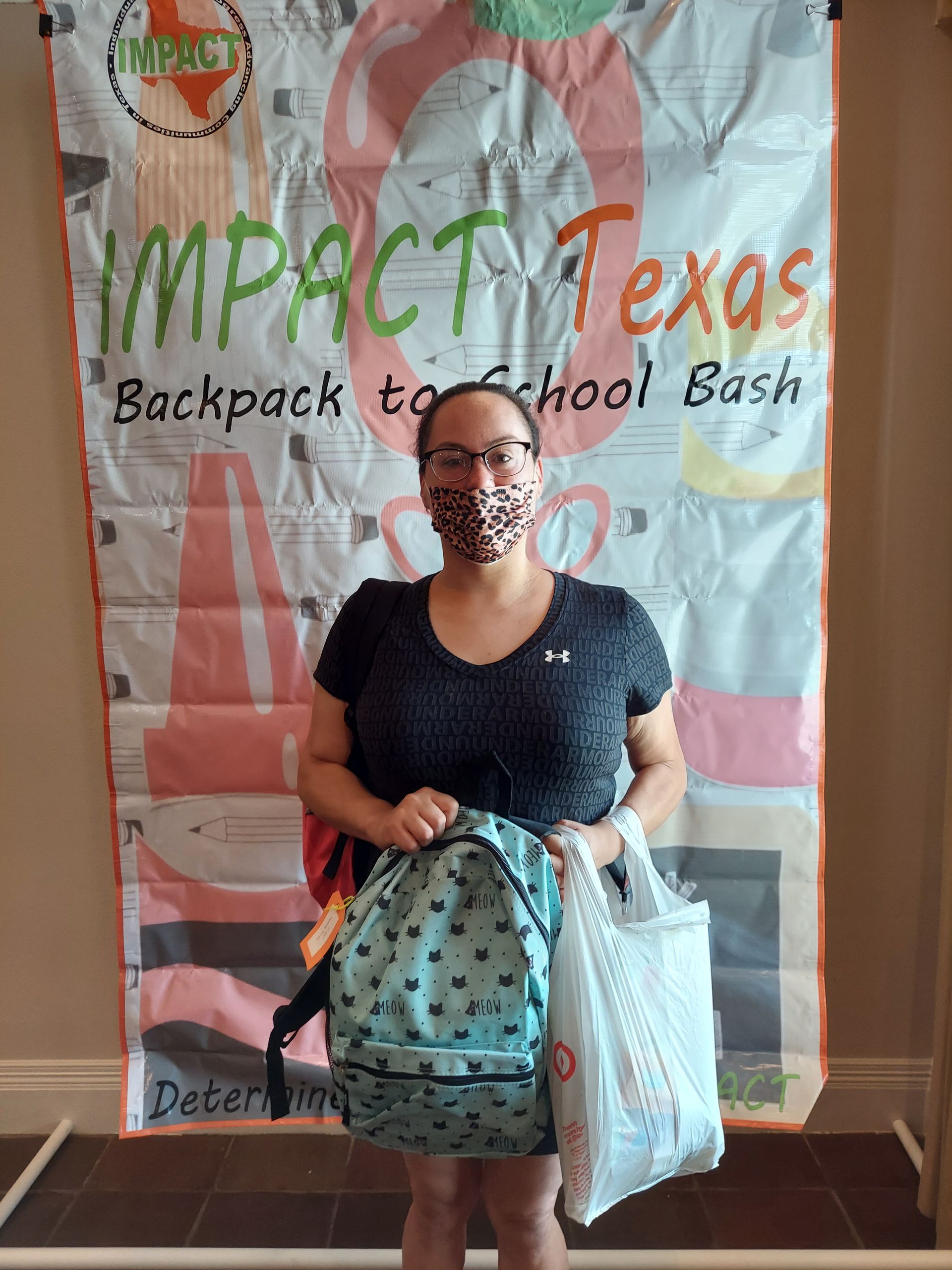 Woman with face mask holding a backpack and a bag, standing in front of an IMPACT Texas banner.