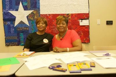 Two women at a table with papers, in front of a Texas flag quilt.