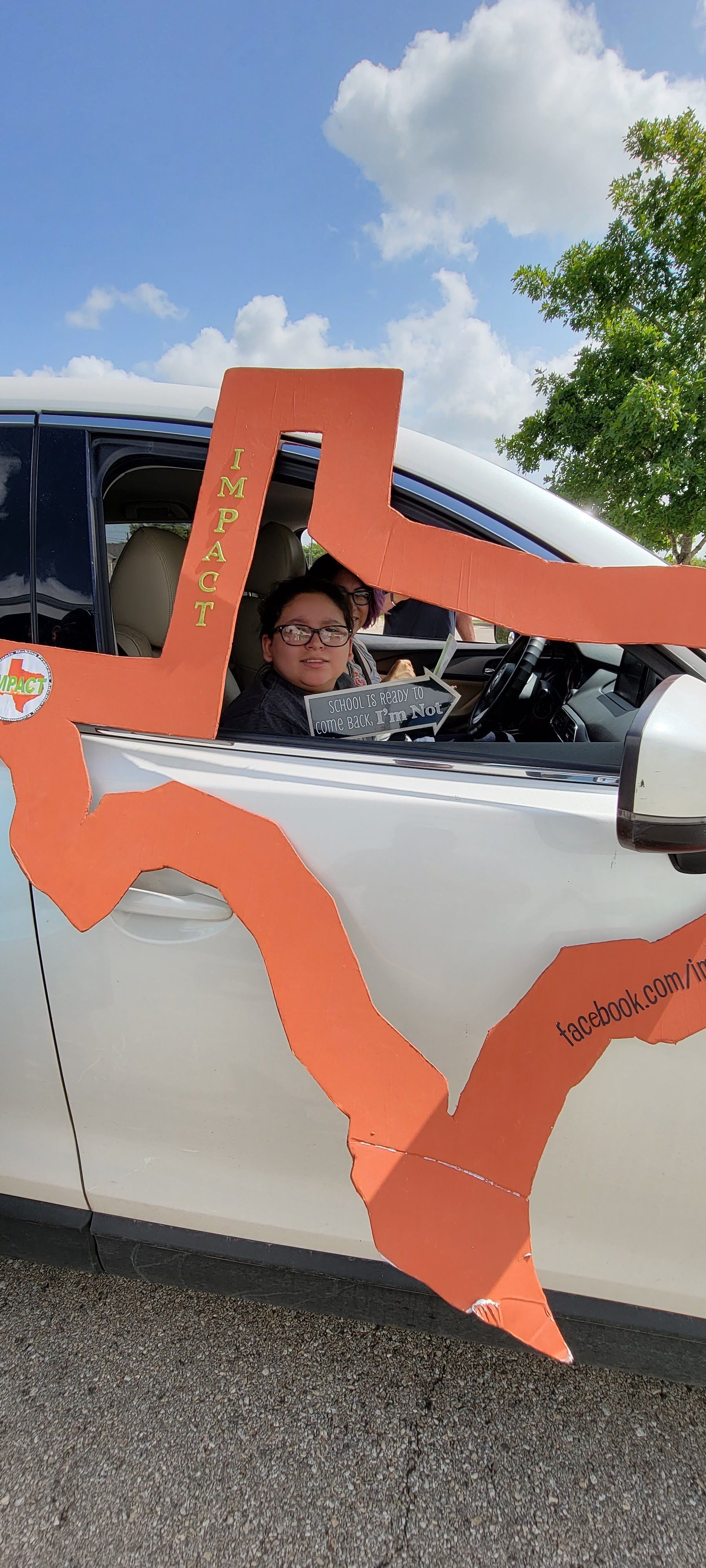 Person in car decorated with orange paper; blue sky and trees in background.