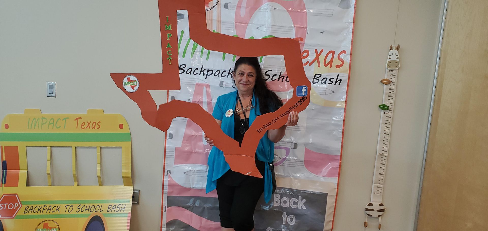 Woman framed by a Texas cutout, in front of a backdrop, near a yellow school bus cut out and a giraffe decoration.