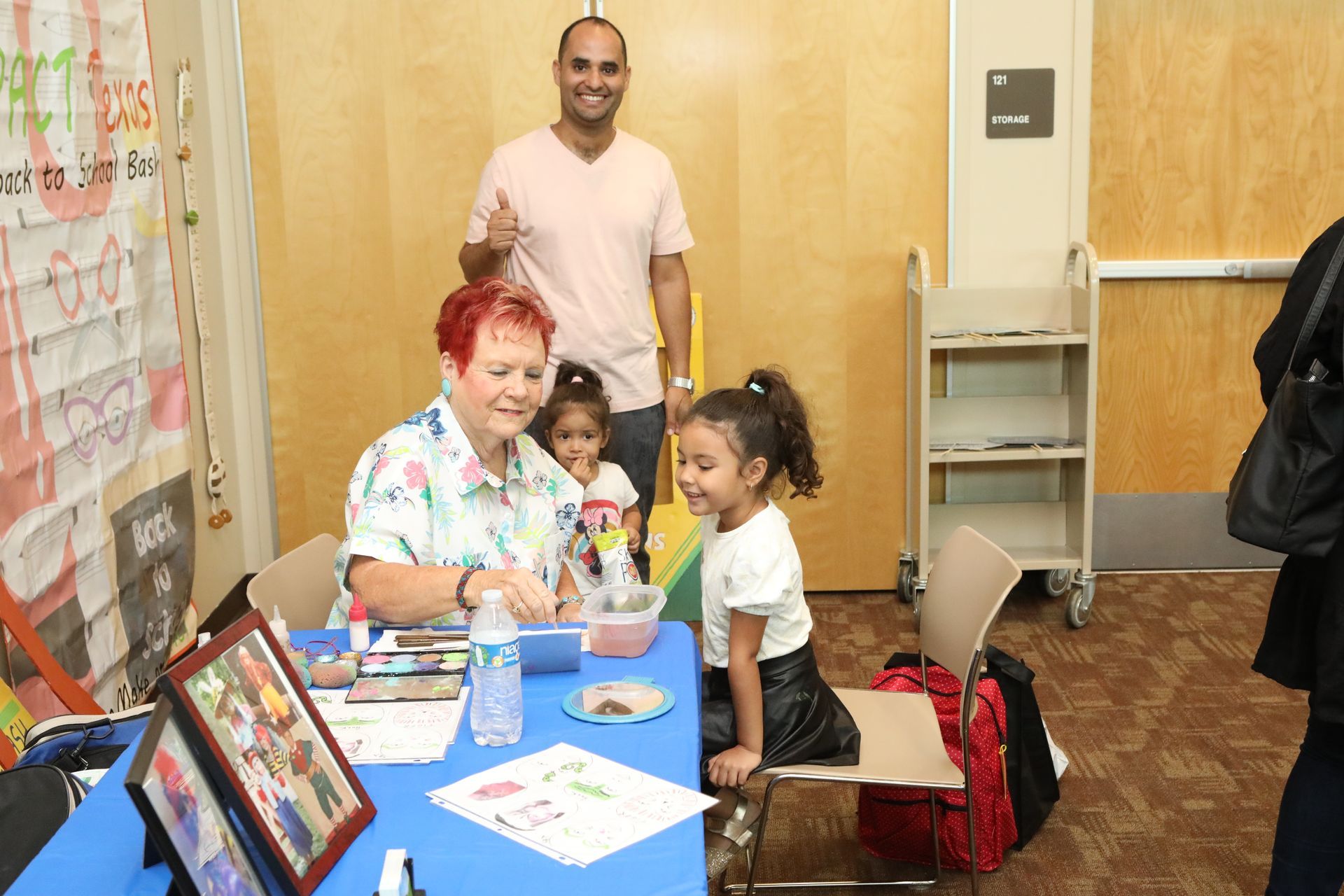 Person coloring with children at a table, man smiles with thumbs up. Inside.