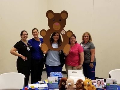 Five healthcare workers pose with a bear cutout and medical supplies.