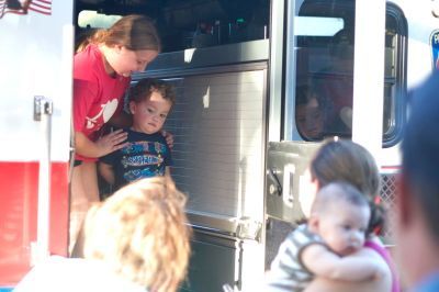 A woman helps a child into a fire truck. Other children and adults are nearby.