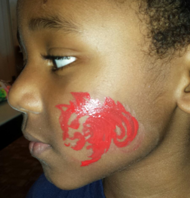 Child with red face paint of a lion on their cheek, indoors.