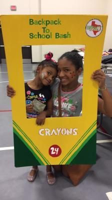 Two girls smiling through a yellow Crayola-themed photo frame at a 