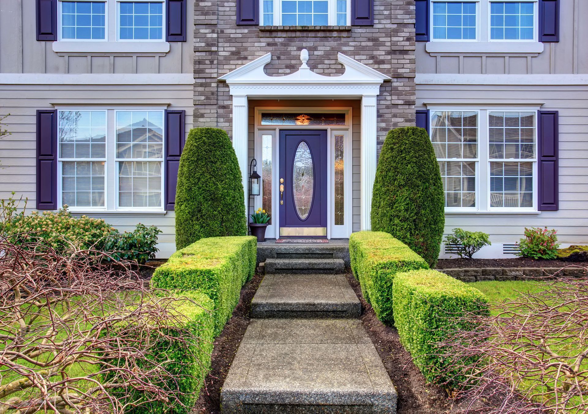 A house with a purple door, brick facade, and trimmed bushes leading up to the entrance.