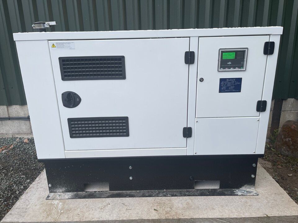 A white generator is sitting on a concrete platform in front of a green building.