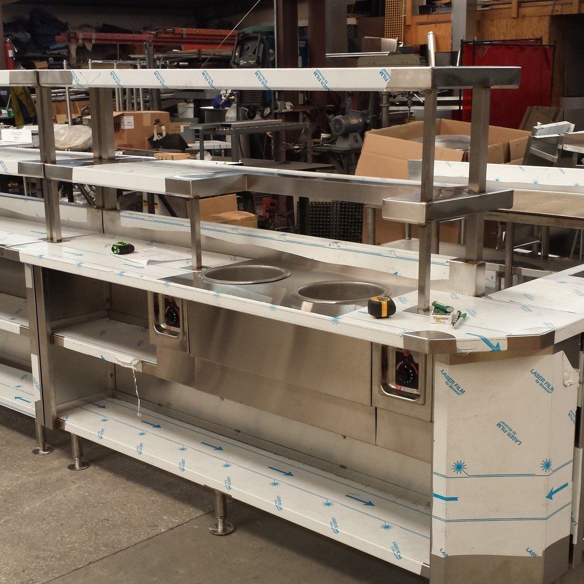 A stainless steel counter with a sink and shelves in a warehouse.