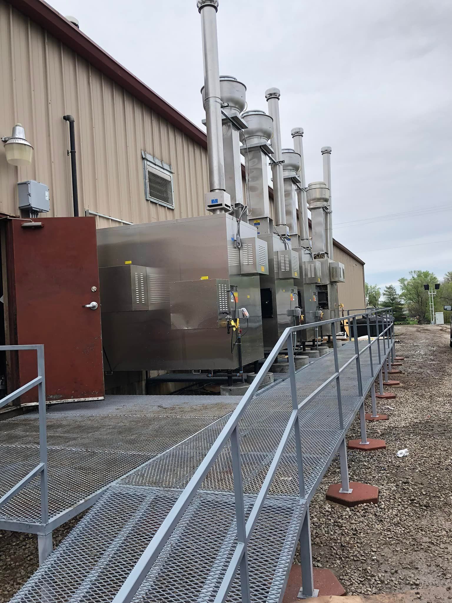 A metal walkway leading to a building with a lot of smoke stacks.