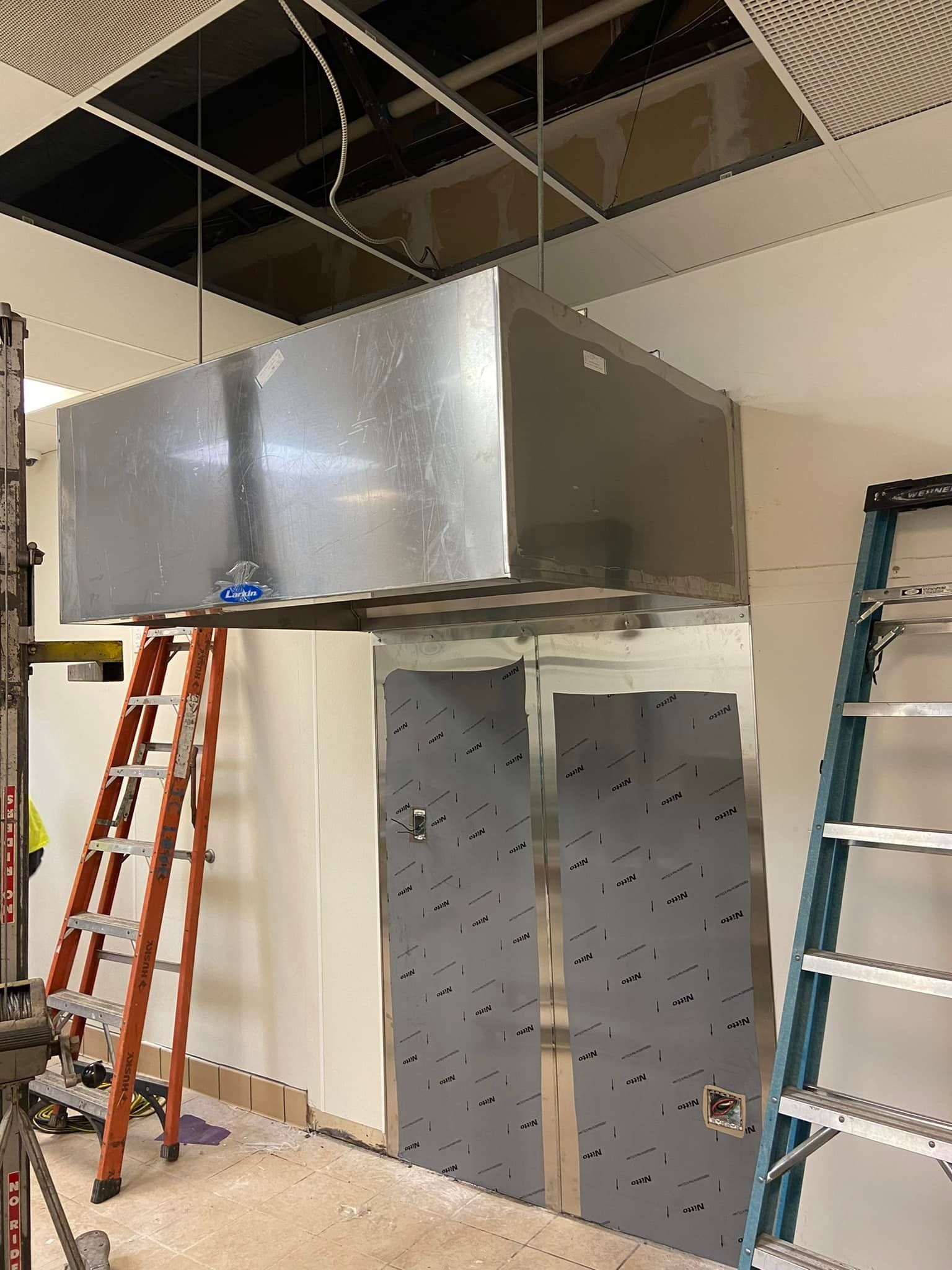 A room with a ladder and a large metal box hanging from the ceiling.