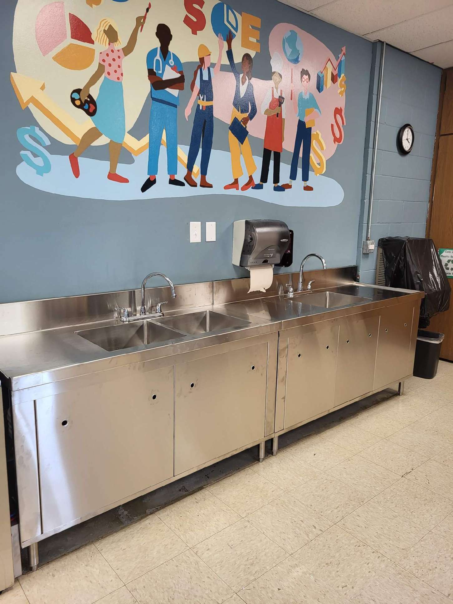 A kitchen with stainless steel sinks and a mural on the wall.