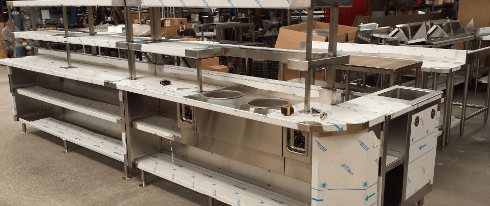 A row of stainless steel counter tops and sinks in a warehouse.