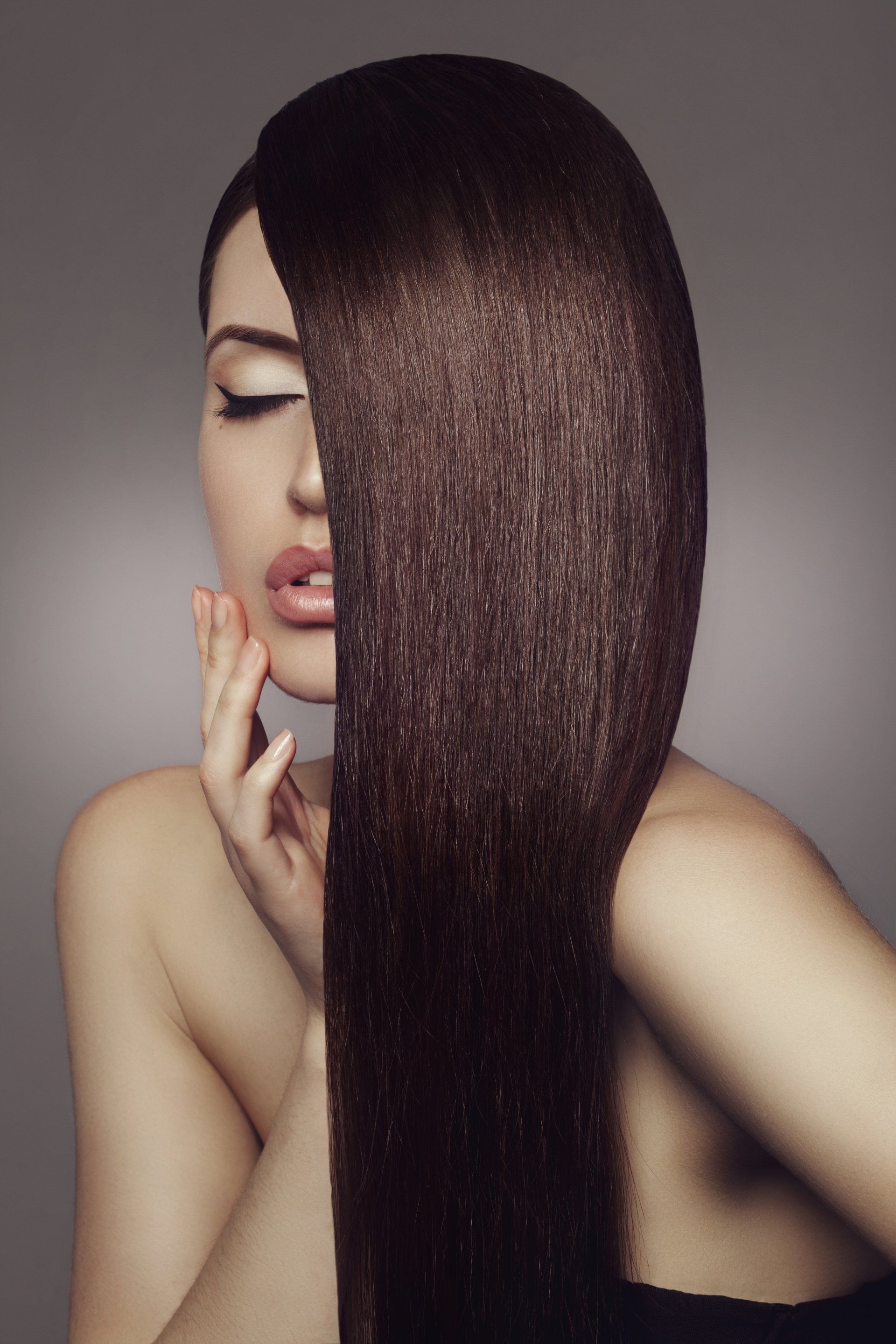 A woman with long brown hair is covering half of her face with her hand.