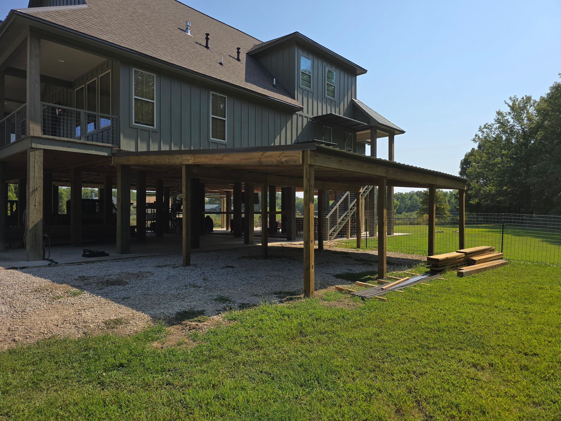 Two-story house with a wooden carport; gravel and grass yard on a sunny day.