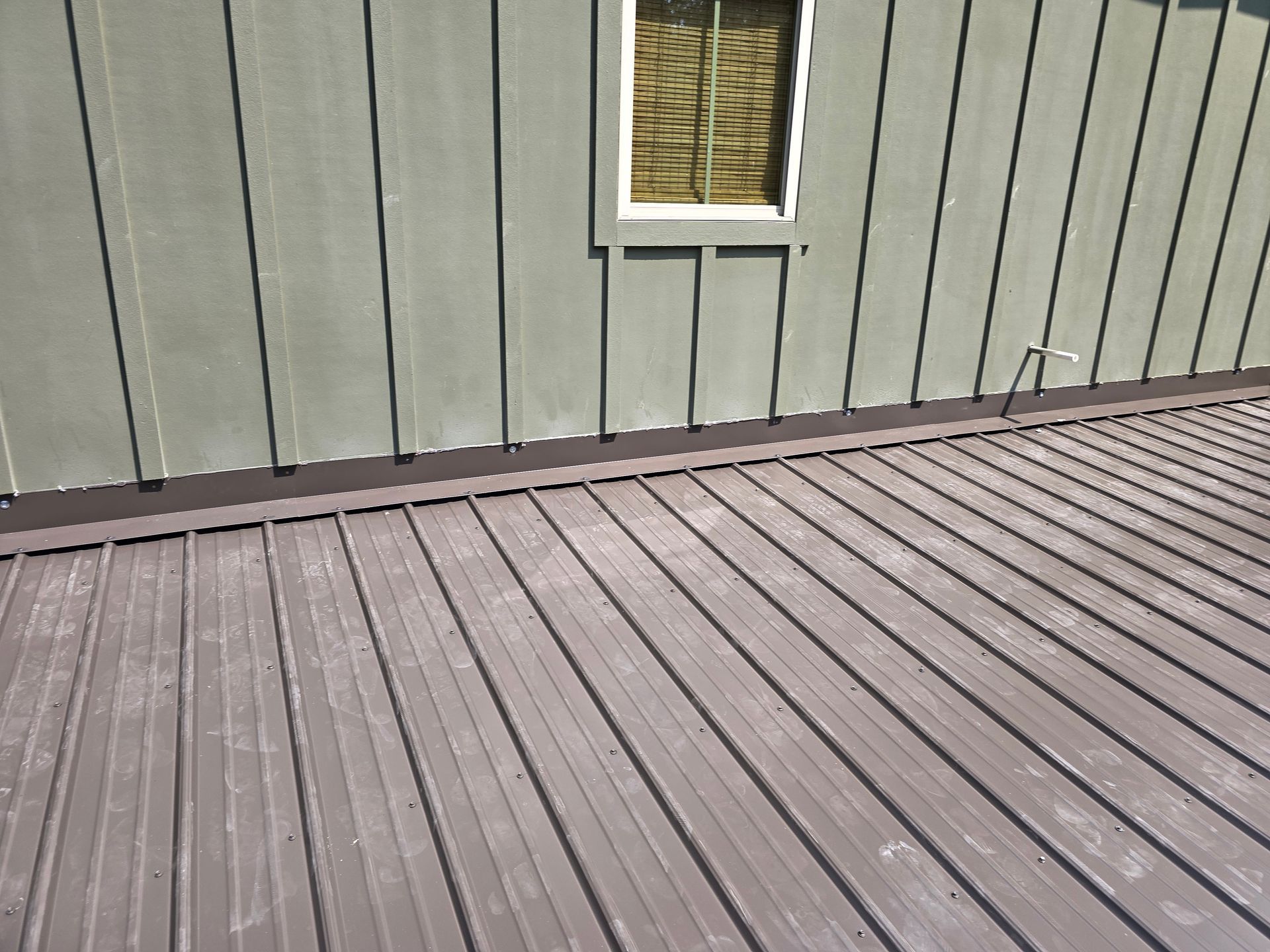 Gray metal roof next to green siding with a small window.