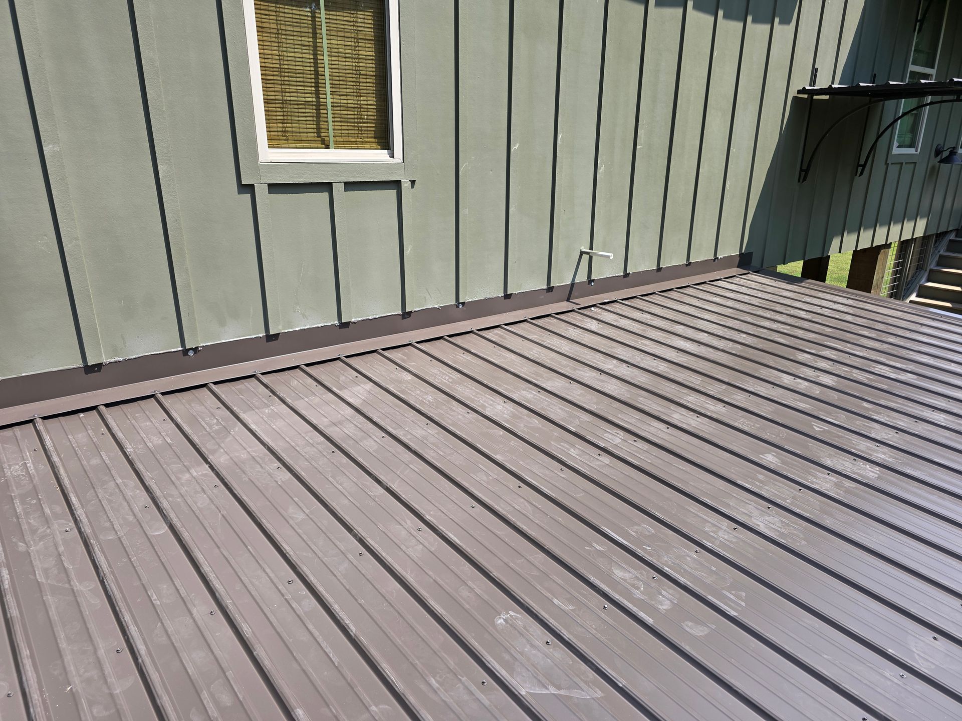 Metal roof of a building with light green siding and a window.