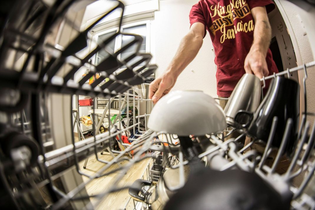 Person loading a white bowl into a dishwasher. Other dishes and metal containers are in the rack.