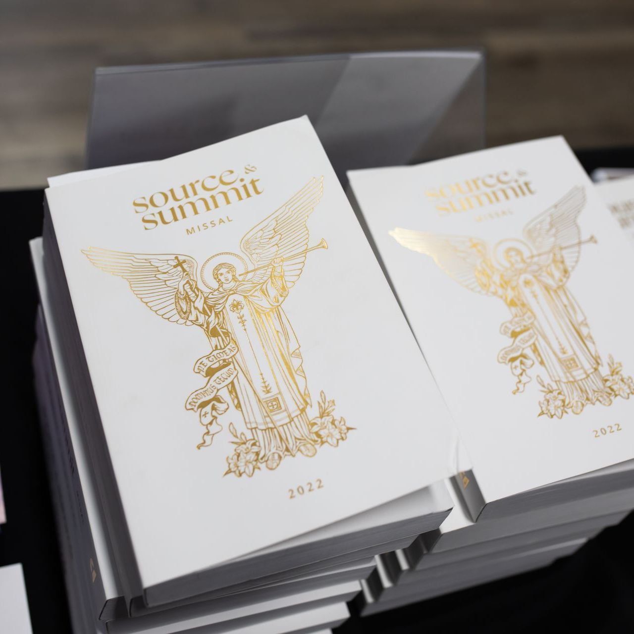 Stacked white booklets with gold angel artwork and the title “source summit” on the cover.