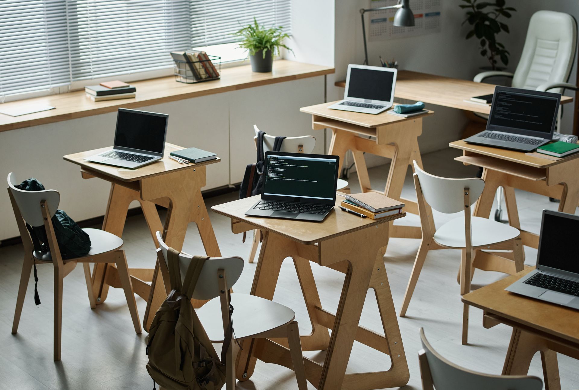 Modern office with several laptops on wooden desks in a bright room with large windows.