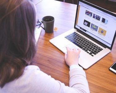 Person using a laptop at a wooden table with a coffee mug nearby
