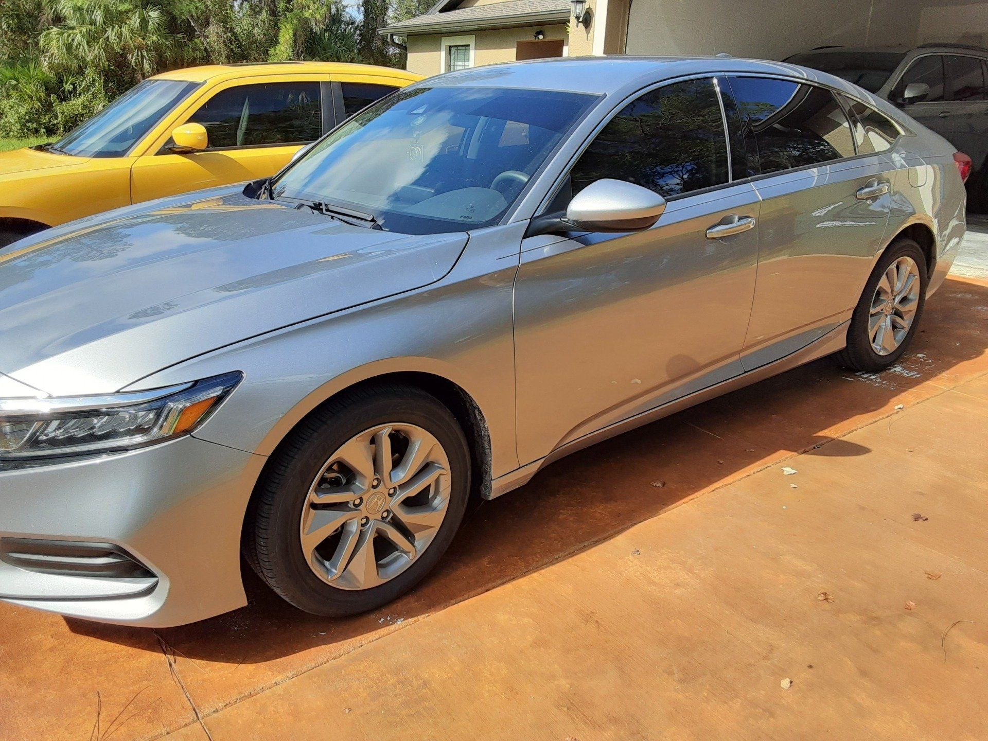 A silver car is parked in a driveway next to a yellow car.