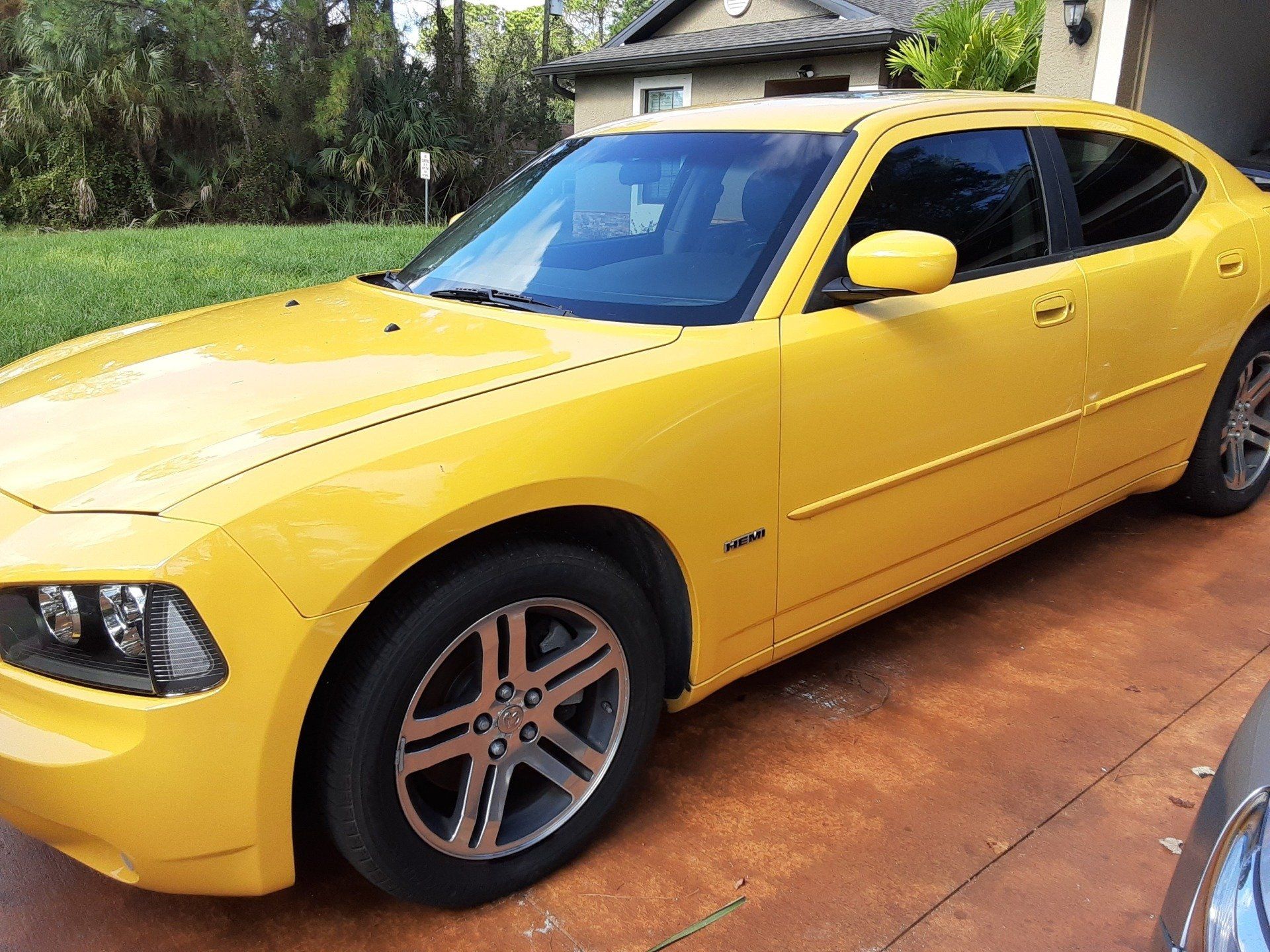 A yellow dodge charger is parked in front of a house