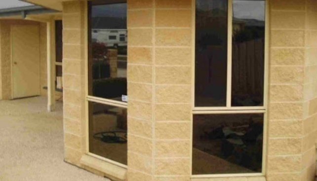 A corner of a house with two windows and a brick wall