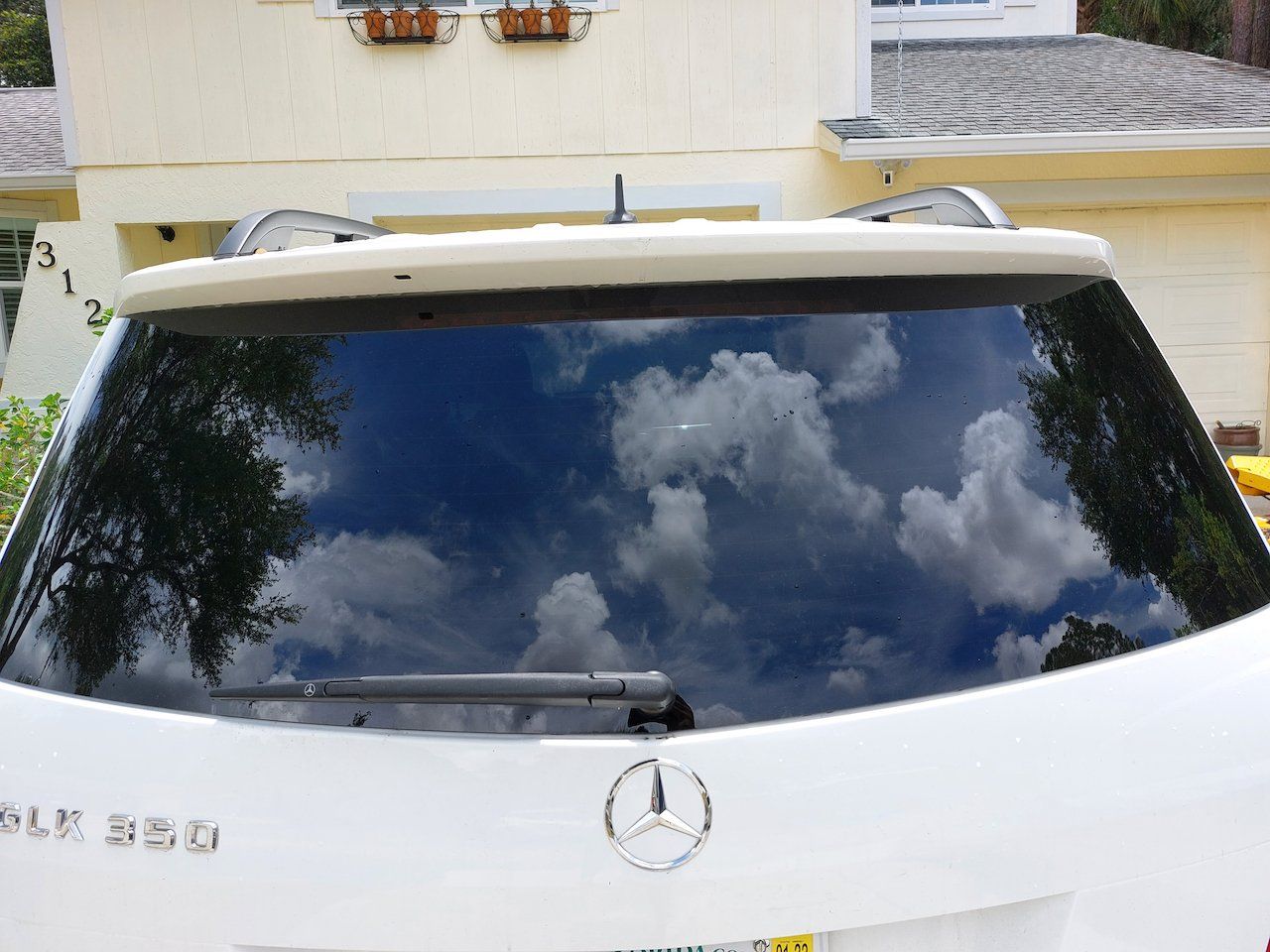 The back of a white mercedes benz suv with a cloudy sky reflected in the windshield