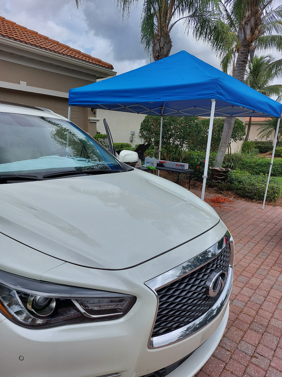 A white car is parked in front of a blue canopy.