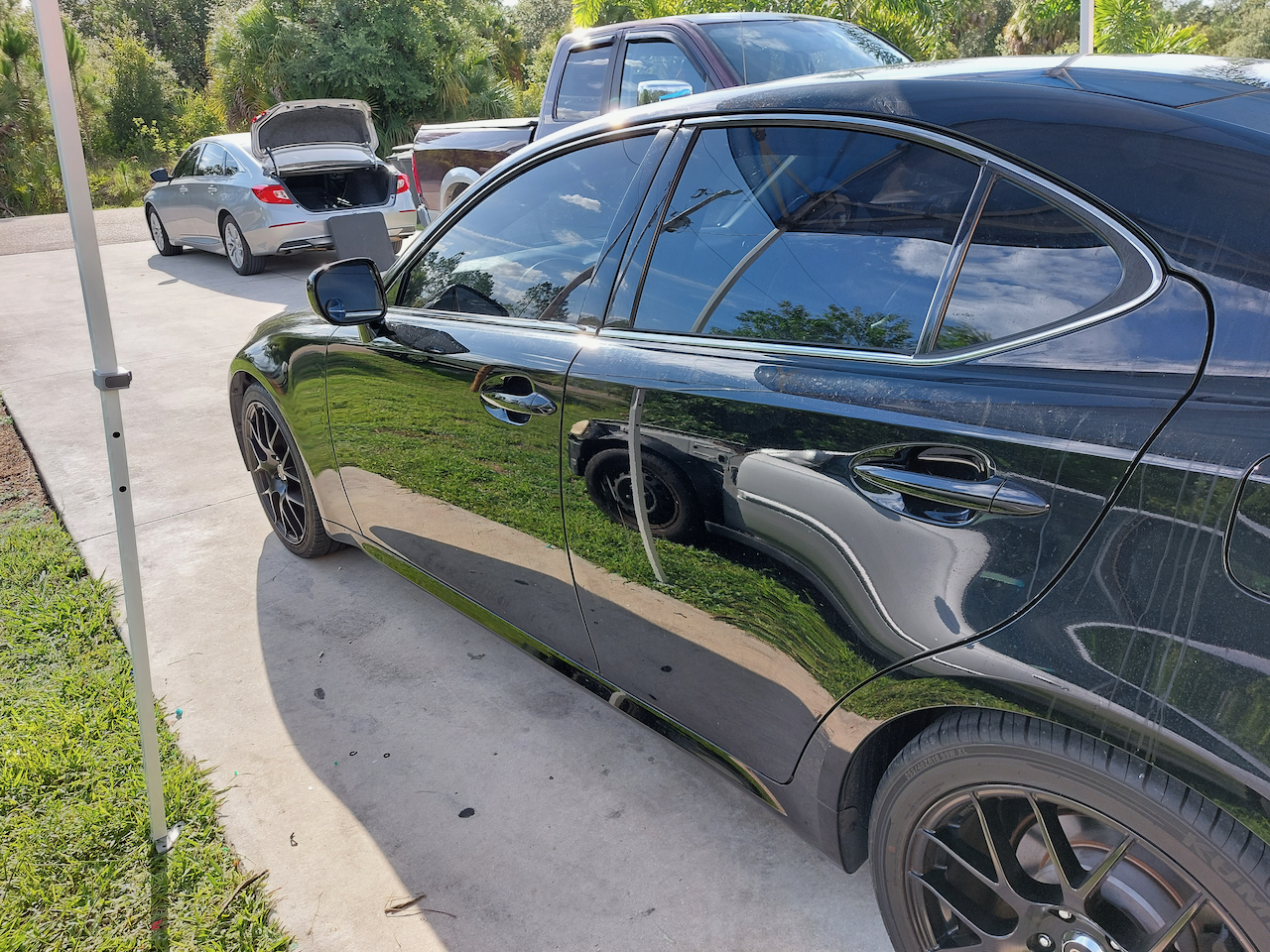 A black car is parked in a driveway next to other cars.