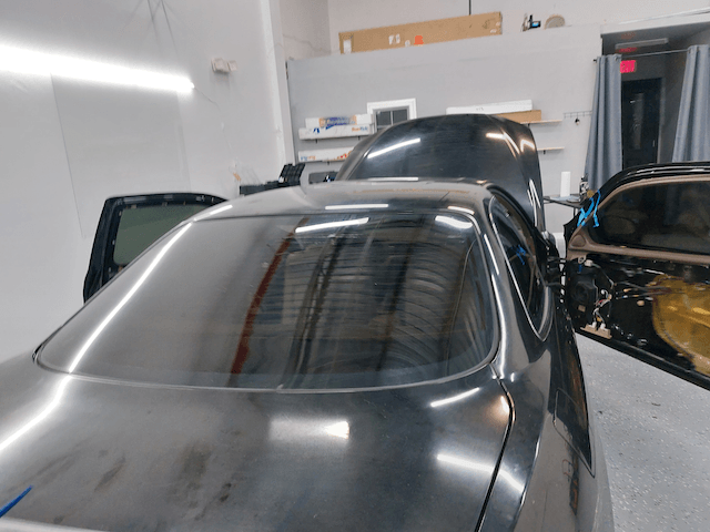 A black car with the hood up is in a garage