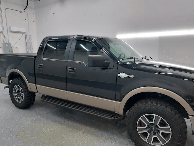 A black and tan pickup truck is parked in a garage.