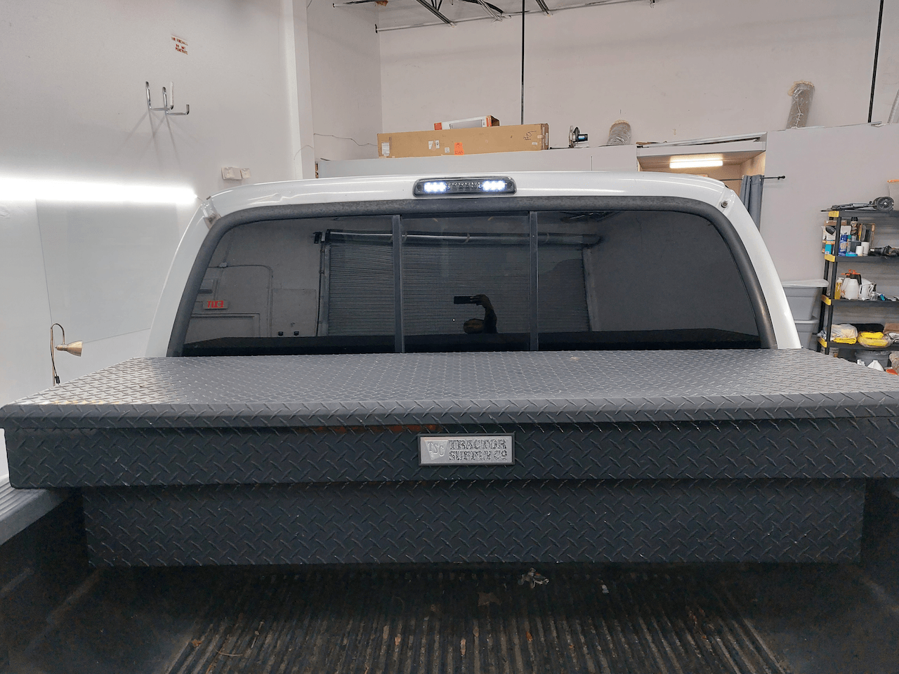 A white truck with a black bed cover is parked in a garage.