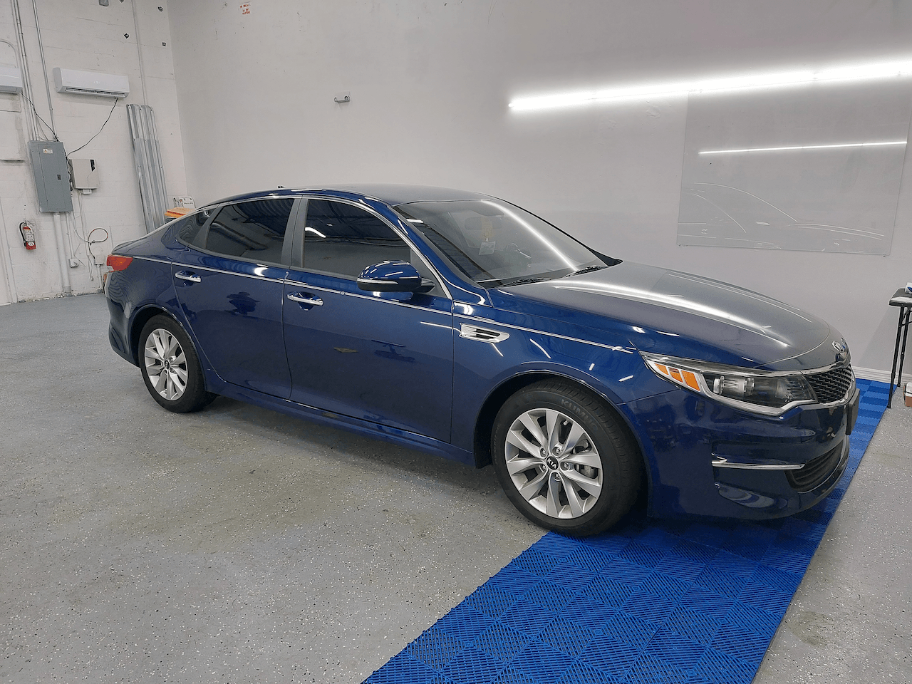 A blue car is parked in a garage on a blue mat.
