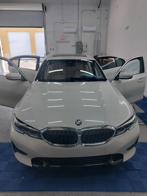 A white bmw 3 series is parked in a garage with its doors open.