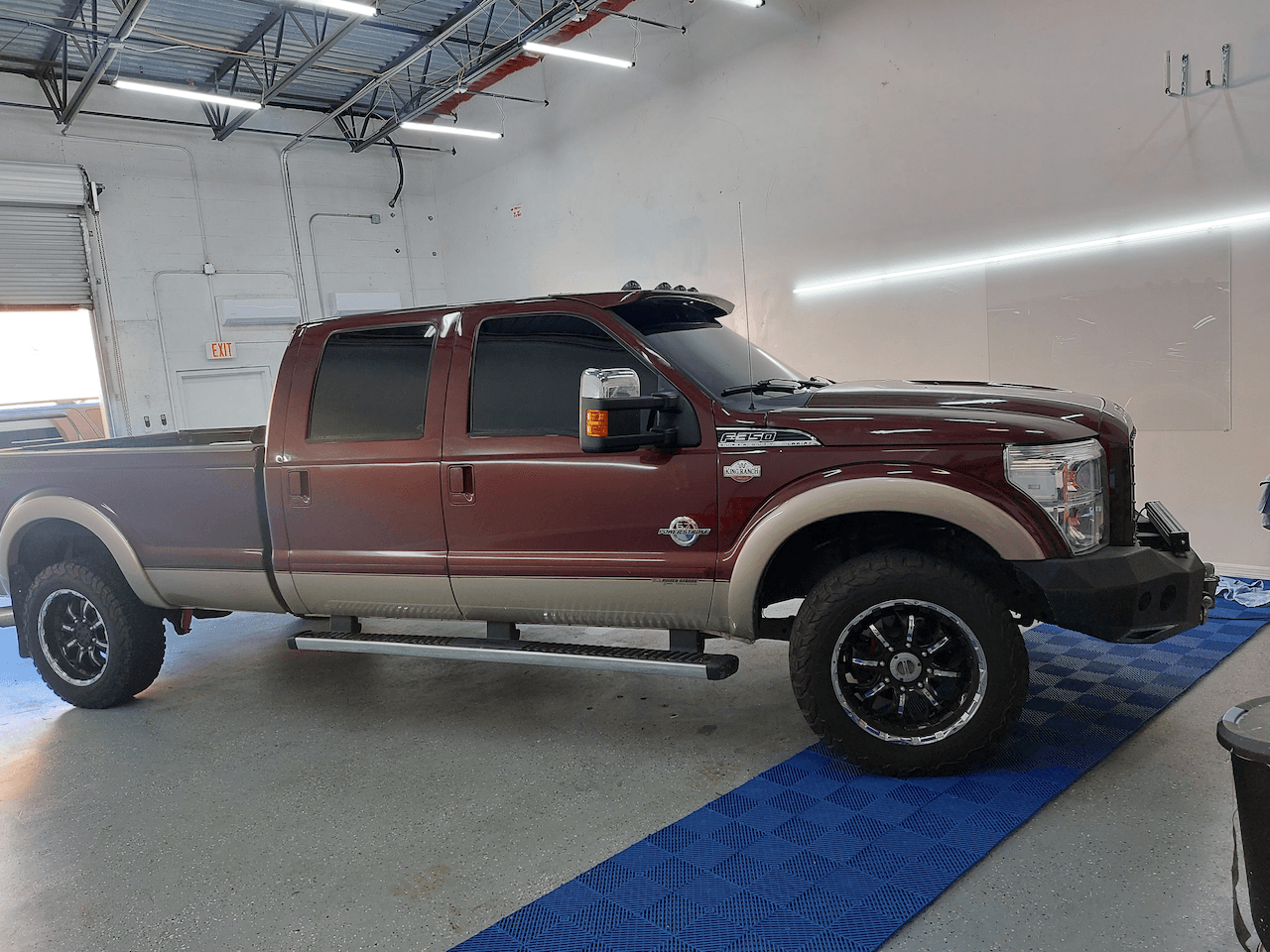 A red truck is parked in a garage next to a blue mat.