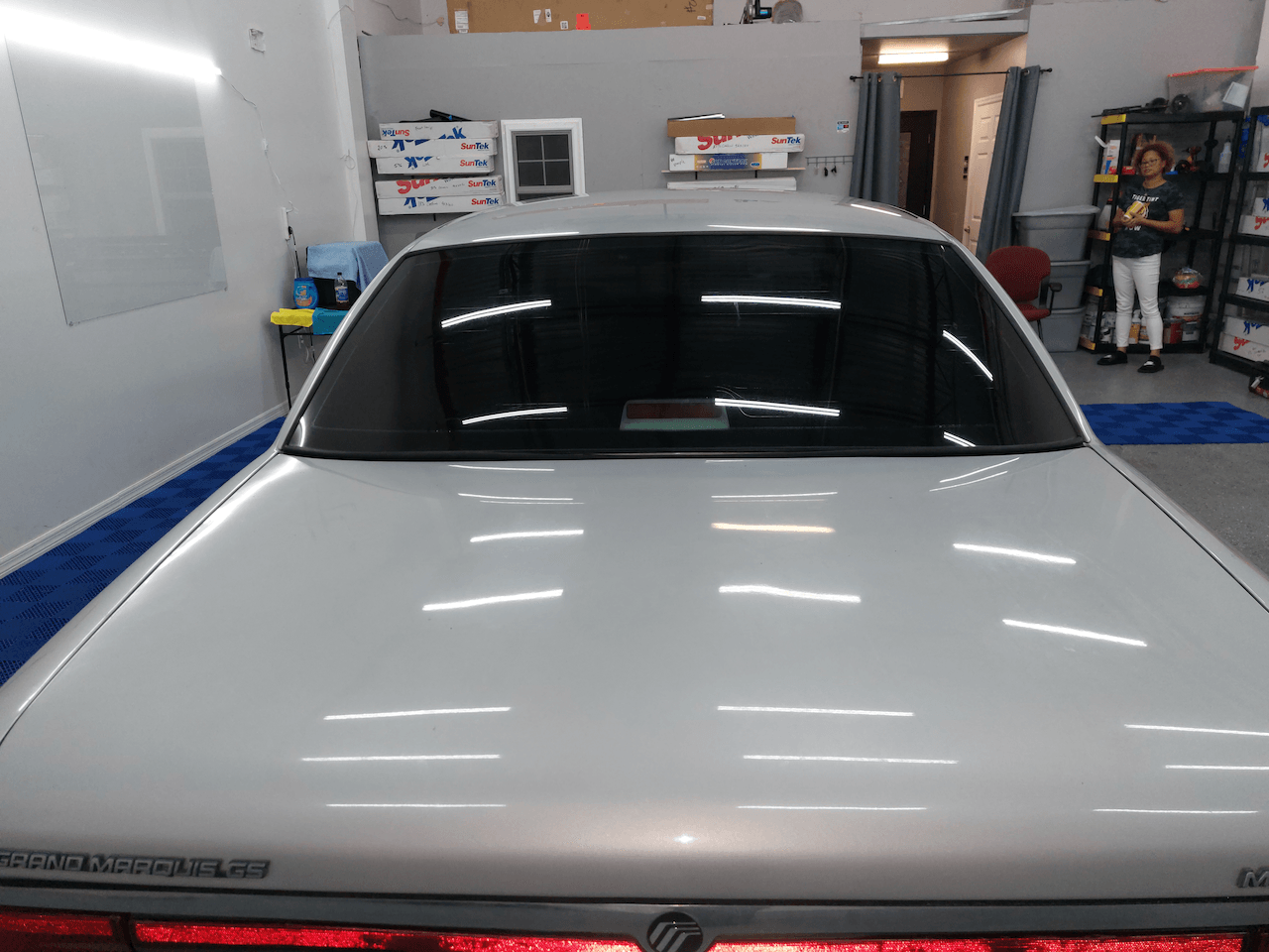 A white car is parked in a garage with a woman standing behind it
