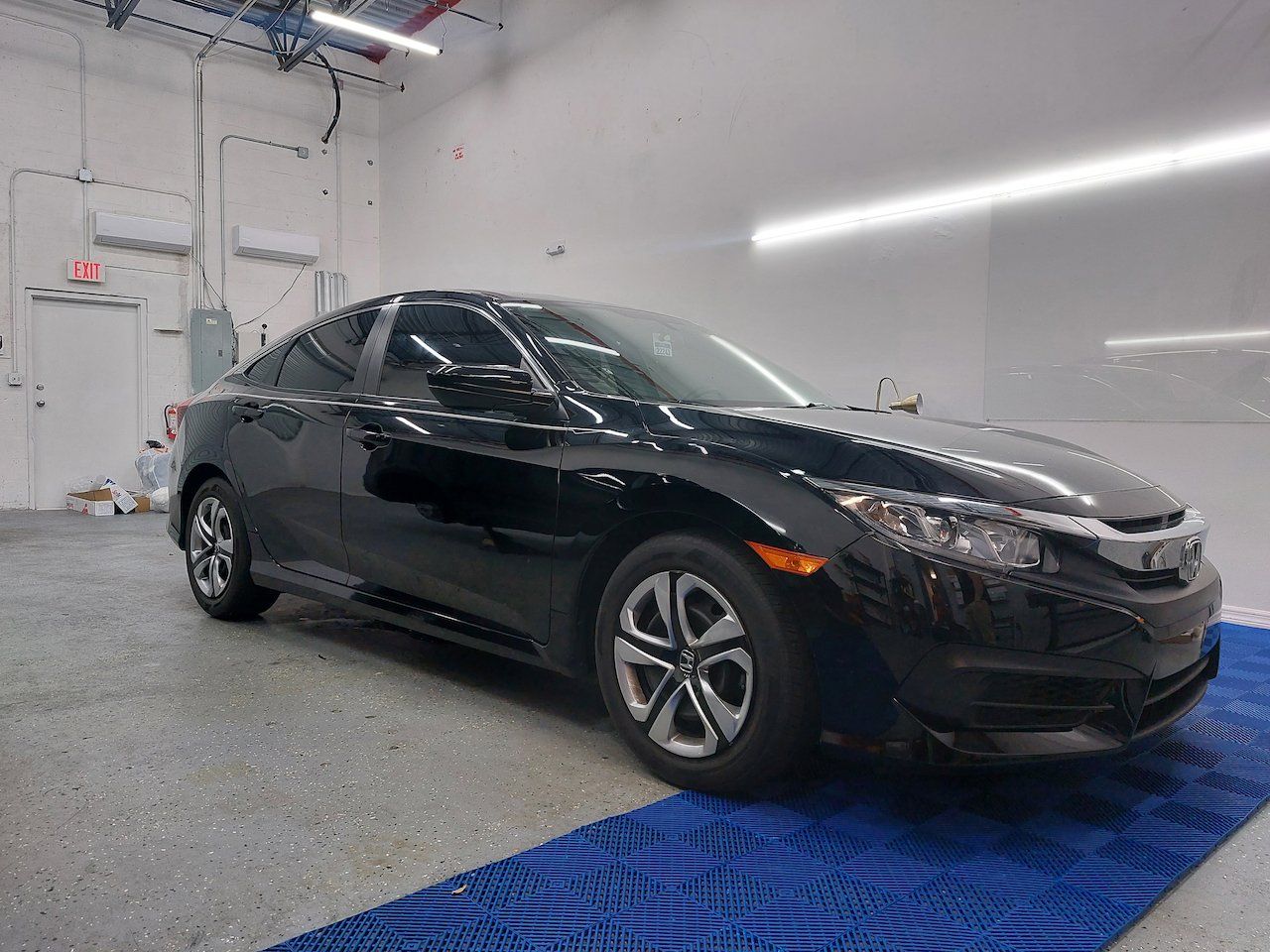 A black honda civic is parked on a blue mat in a garage.