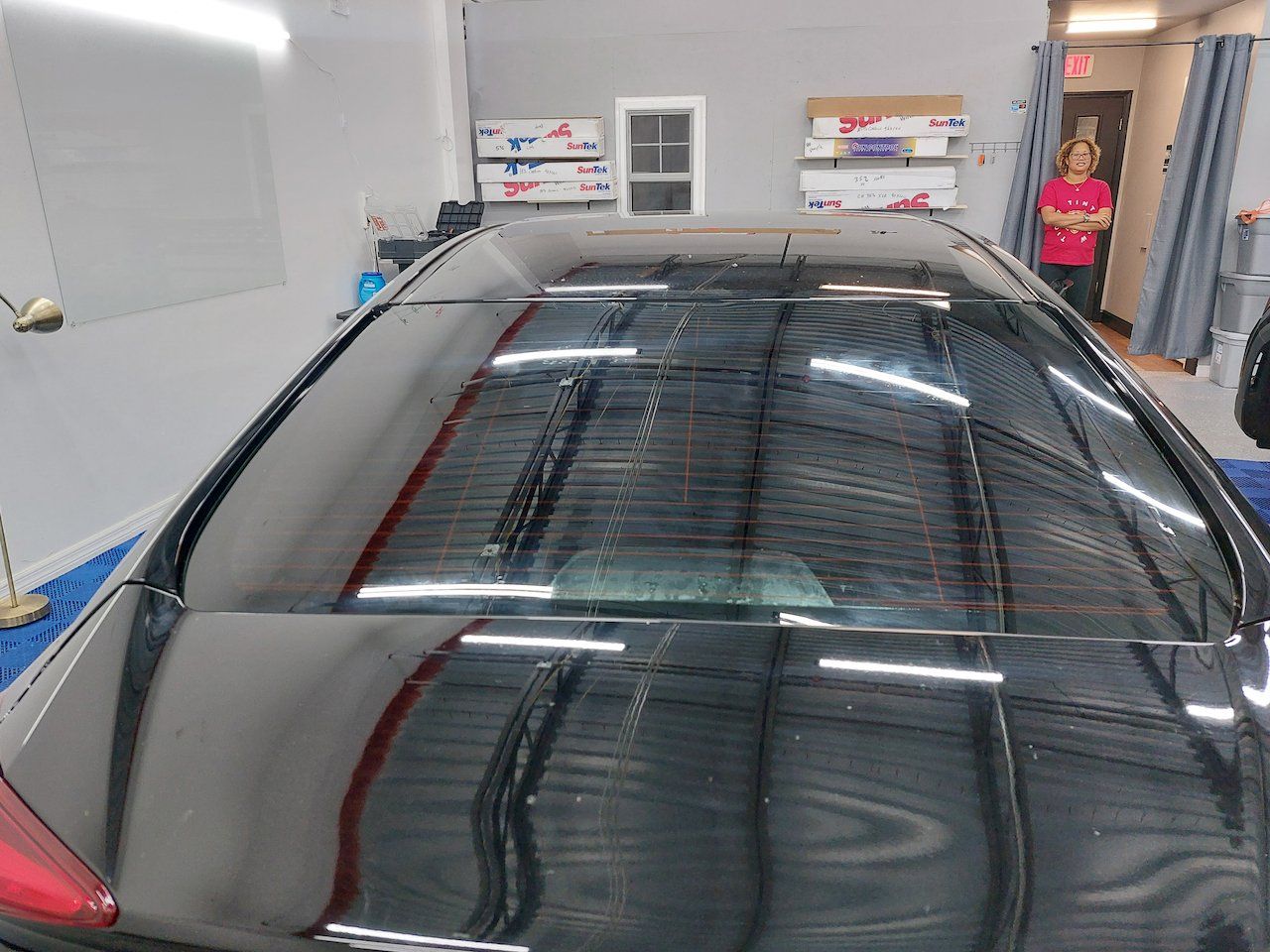 A black car is parked in a garage with a woman standing in the background.